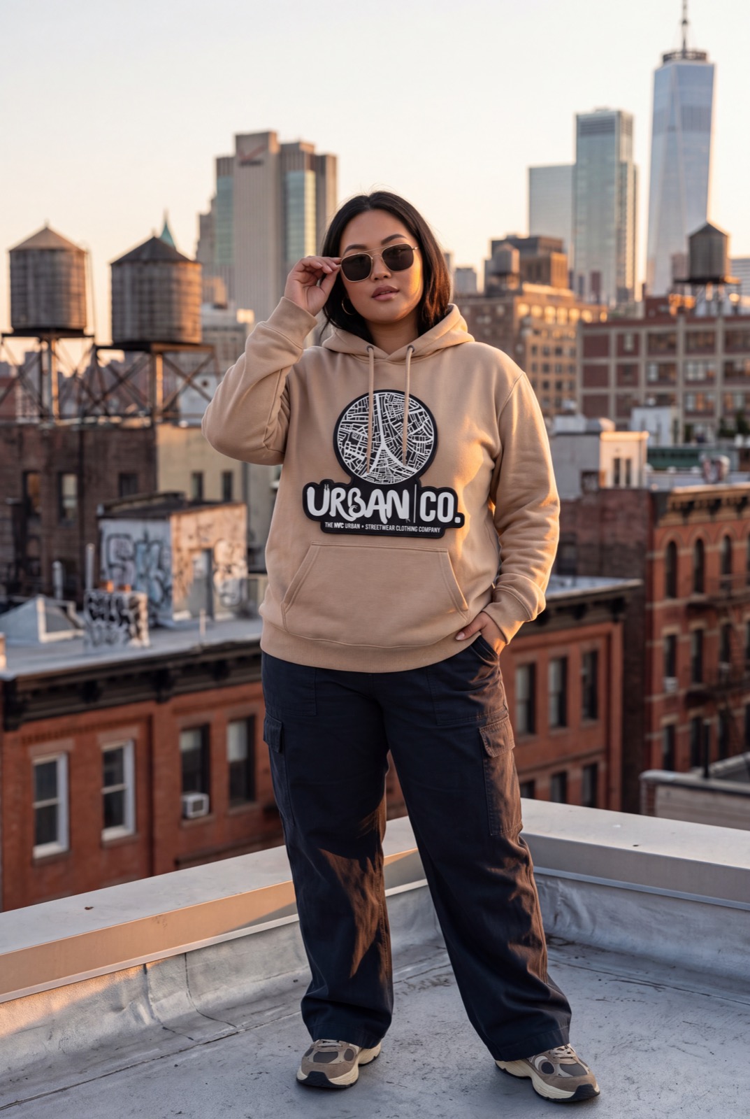 Woman wearing an Urban Co. beige hoodie on a NYC rooftop at sunset
